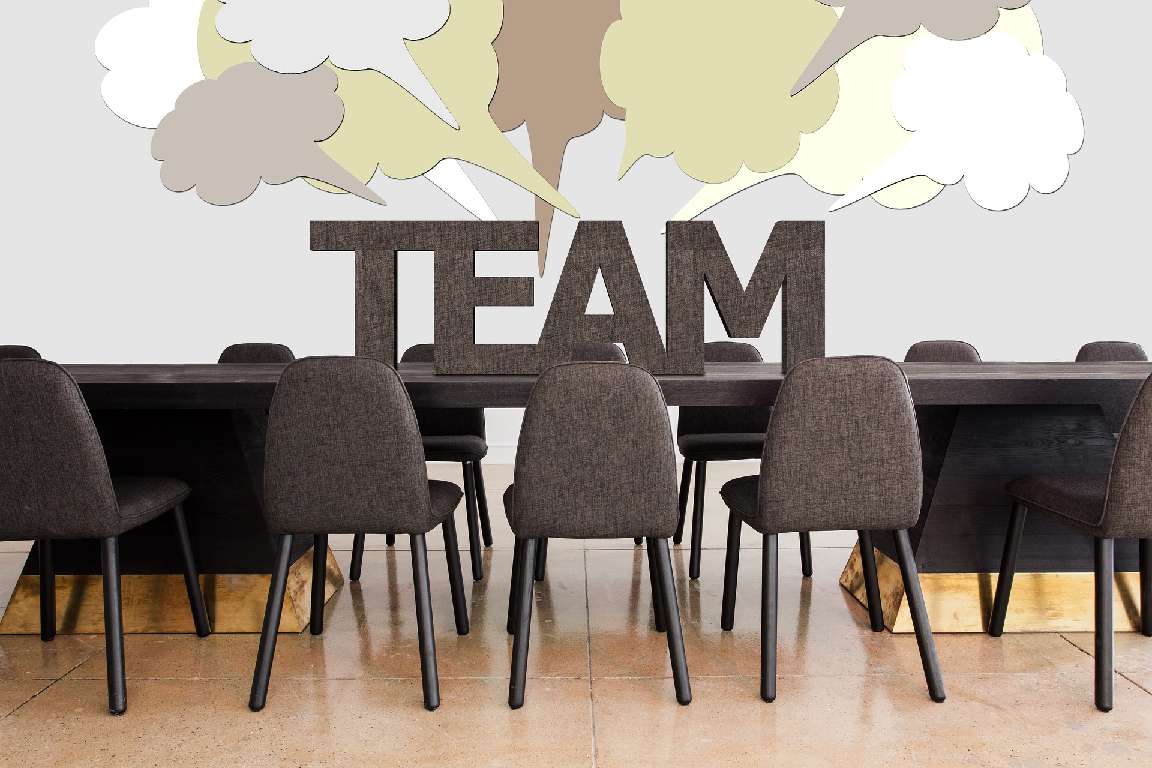 Stühle am Tisch mit dem Wort "TEAM" im Hintergrund.